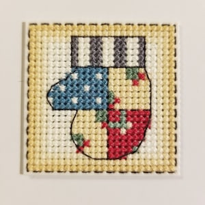 Puede incluir: Un diseño de punto de cruz de una manopla colorida con un puño a rayas. La manopla está compuesta por cuatro cuadrados con diferentes patrones: lunares, rayas, un patrón floral y un patrón rojo y verde.