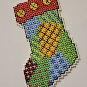 May include: A colourful patchwork Christmas stocking with a red cuff and three yellow buttons. The stocking is made of green, blue, yellow, and red fabric.