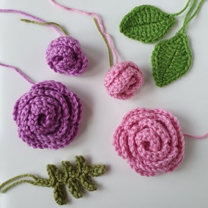 Pu&ograve; includere: Un set di fiori e foglie all'uncinetto in tonalit&agrave; di rosa, viola e verde. I fiori sono realizzati con un motivo a spirale e le foglie sono semplici e delicate.