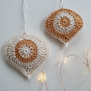 May include: Two crocheted ornaments in the shape of a teardrop with a white background and a yellow center. The ornaments are hanging from white string.