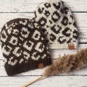 May include: Two brown and white leopard print knit hats with a brown leather tag that says "Knitshed".