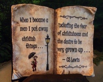 May include: An open book with aged paper pages, featuring a quote by C.S. Lewis. The left page reads "When I became a man I put away childish things..." with an illustration of a child with an umbrella. The right page continues the quote.
