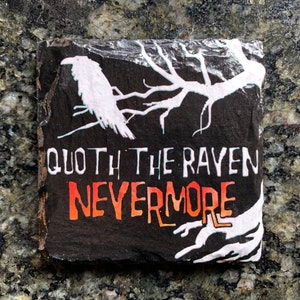 Könnte beinhalten: Quadratischer, schwarzer Schieferuntersetzer mit weißer Rabenillustration und Astdesign. Der Text "Quoth the Raven Nevermore" ist in Weiß und Orange gehalten. Die Kanten sind rau und natürlich.