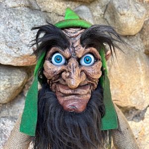 Op de afbeelding: Handgemaakte pop met een leprechaun-ontwerp. De pop heeft een gedetailleerd gezicht met blauwe ogen, een lange zwarte baard en een groene hoed. Het lichaam van de pop is gemaakt van jute, wat hem een rustieke uitstraling geeft.