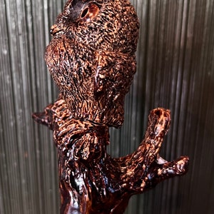 May include: A detailed, brown wooden carving of an owl perched on a branch. The owl has textured feathers and large, round eyes. The branch has a rough, natural appearance, with a glossy finish.