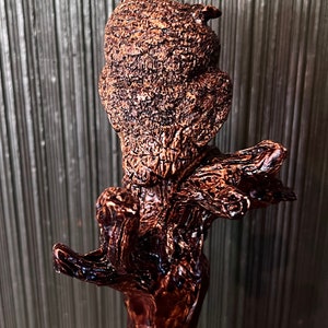 May include: A detailed, brown, carved wooden owl figurine perched on a branch. The owl has textured feathers and a focused gaze. The wood has a glossy finish, and the sculpture is set against a neutral background.