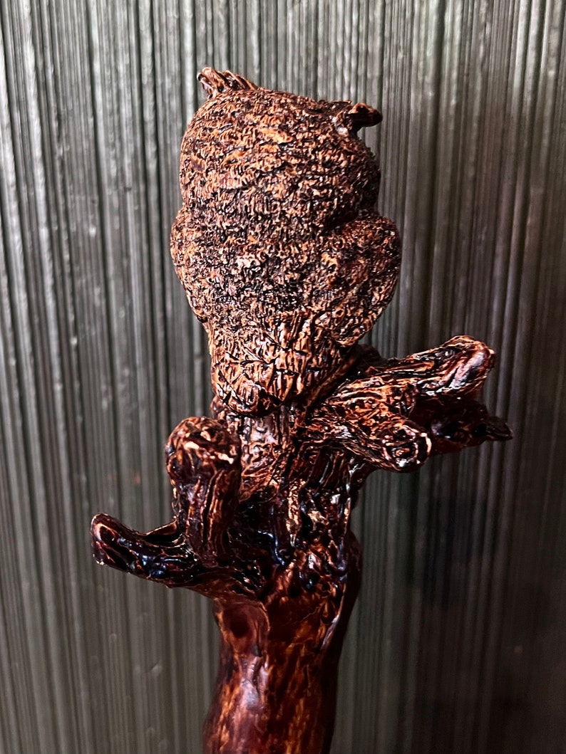 May include: A detailed, brown, carved wooden owl figurine perched on a branch. The owl has textured feathers and a focused gaze. The wood has a glossy finish, and the sculpture is set against a neutral background.