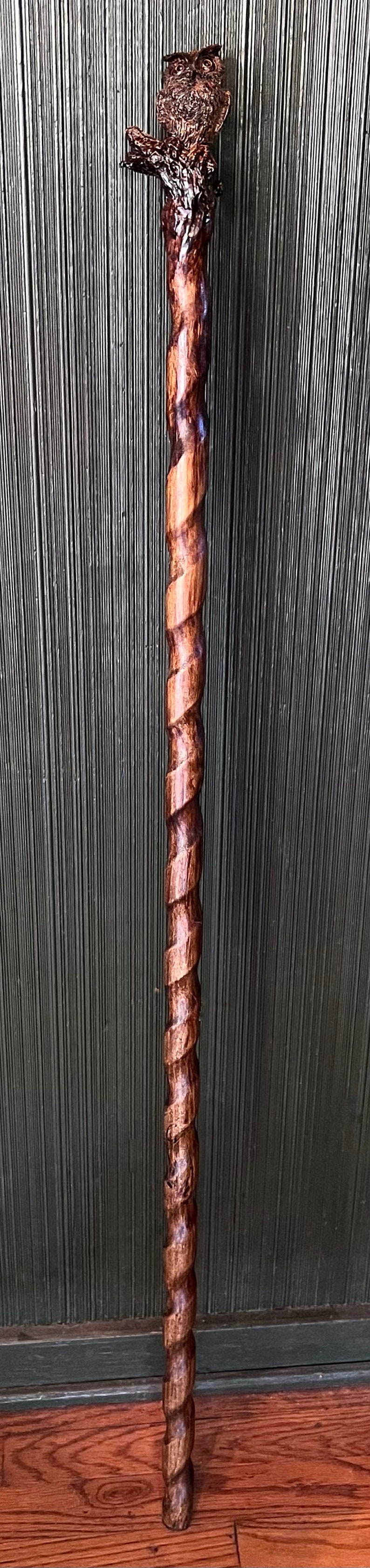 May include: A handcrafted wooden walking stick with a carved owl head and a spiral design. The stick is made of dark brown wood and measures approximately 36 inches in length.
