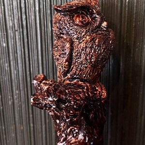 May include: A detailed, brown wooden carving of an owl perched on a branch. The owl has textured feathers and large, detailed eyes. The carving is a rich, dark brown color, with a glossy finish.