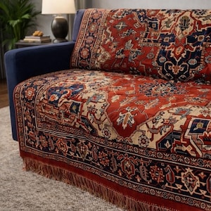 Op de afbeelding: Een rood, marineblauw en beige patroon op een bankhoes met een gefranjerde rand. De hoes is over een blauwe bank gedrapeerd en toont een ingewikkeld, traditioneel ontwerp. Het tapijtachtige textiel voegt een vleugje elegantie toe.