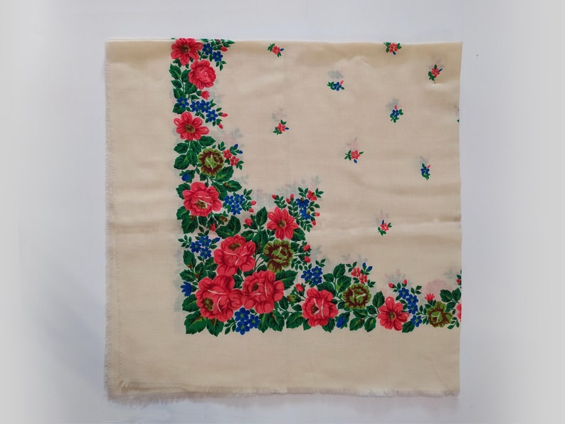 Pode incluir: Um len&ccedil;o quadrado branco com um padr&atilde;o floral. A borda do len&ccedil;o &eacute; decorada com flores vermelhas, cor-de-rosa, verdes e azuis. O centro do len&ccedil;o &eacute; de cor branca s&oacute;lida.