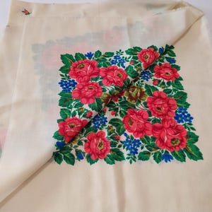 Pode incluir: Um len&ccedil;o de algod&atilde;o branco com um design floral. O design apresenta rosas vermelhas, folhas verdes e flores azuis. O len&ccedil;o tem uma borda franjada.