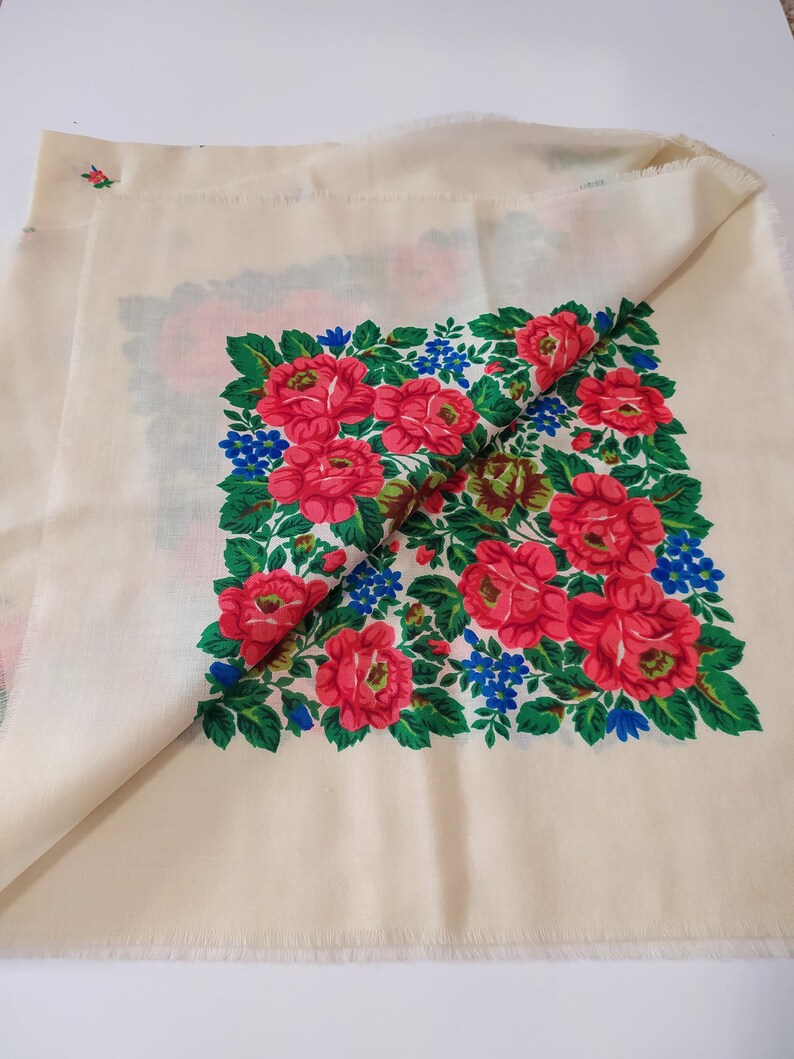 Pode incluir: Um len&ccedil;o de algod&atilde;o branco com um design floral. O design apresenta rosas vermelhas, folhas verdes e flores azuis. O len&ccedil;o tem uma borda franjada.