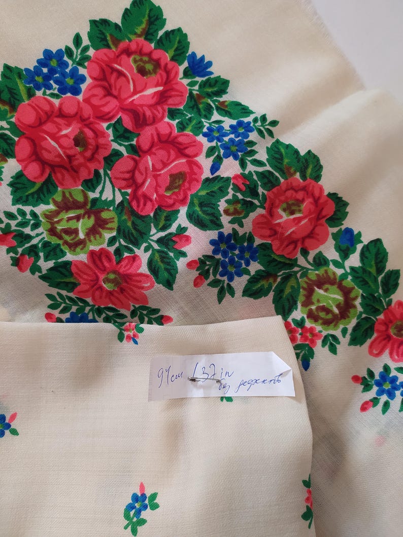 Pode incluir: Um tecido branco com um padr&atilde;o floral de rosas vermelhas e flores azuis. O tecido tem 91 cm (32 polegadas) de largura.