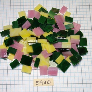 May include: A pile of small, square glass tiles in shades of green, yellow, and pink. The tiles are arranged in a random pattern and are ready for use in a mosaic project.
