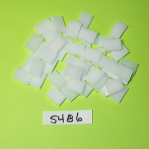 Puede incluir: Un conjunto de pequeñas baldosas rectangulares blancas dispersas sobre un fondo verde brillante. También hay una pequeña etiqueta blanca con el número "5486". Las baldosas parecen estar hechas de un material liso y opaco.