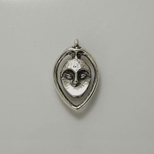 May include: Silver pendant featuring a stylized face with closed eyes, set within a teardrop-shaped frame.