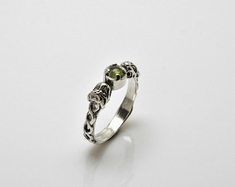 Può includere: Un anello d'argento con una pietra preziosa verde incastonata in un design a nodo celtico.