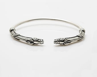 May include: A silver bracelet with two wolf heads at the ends. The bracelet is open and has a simple design.