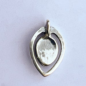 May include: A silver pendant in the shape of a teardrop with a smaller circle inside. The pendant has a smooth, polished finish.