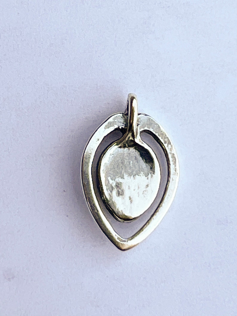 May include: A silver pendant in the shape of a teardrop with a smaller circle inside. The pendant has a smooth, polished finish.