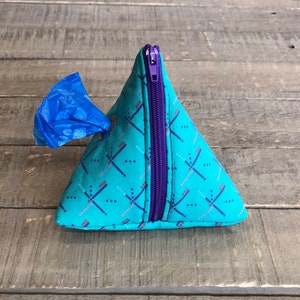 May include: A turquoise blue pyramid-shaped dog waste bag dispenser with a purple zipper and a blue plastic bag sticking out of the opening.