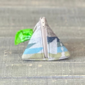May include: A triangular-shaped zippered pouch with a geometric pattern in shades of blue, green, and brown. The pouch is made of fabric and has a zipper closure.