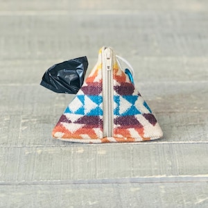 May include: A triangular-shaped, zippered pouch with a colorful geometric pattern. The pouch is made of a soft, woven fabric and has a black plastic bag inside.