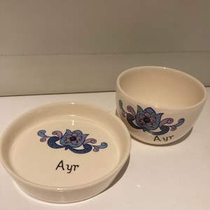 Może przedstawiać: Dwie białe ceramiczne miski z niebieskimi i różowymi wzorami kwiatowymi. Obie miski mają napis "Ayr".