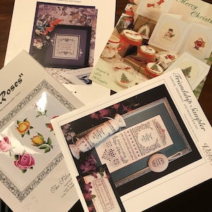 May include: A collection of cross stitch patterns featuring floral designs, including roses, lavender, and a friendship sampler. The patterns are printed on white paper with black text and illustrations.