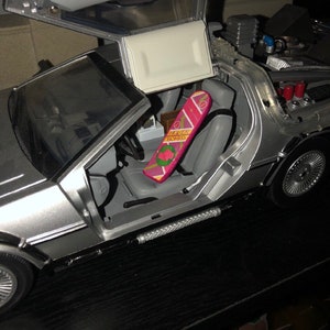 May include: A silver toy car with the doors open, revealing a pink hoverboard with the text "Hover Board" printed on it.