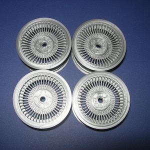 May include: Four silver-colored wire wheels, each with a central hub and numerous spokes radiating outwards. The wheels are arranged in a square formation against a dark blue background, showcasing a detailed design.