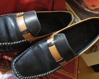 May include: A pair of black leather loafers with tan leather accents. The loafers have a stitched edge and a pointed toe.