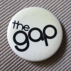 May include: White button with black text that reads "the gap".