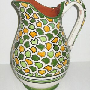 May include: A white ceramic pitcher with a green and orange geometric pattern. The pitcher has a wide mouth and a handle.