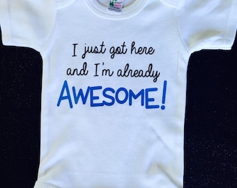 Può includere: Un body bianco per neonato con maniche corte e una grafica blu e nera che dice "Sono appena arrivato e sono già FANTASTICO!"