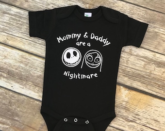 Può includere: Body nero per neonato con testo bianco che recita "Mommy & Daddy are a Nightmare" con un'immagine di cartone animato di Jack Skellington e Sally di The Nightmare Before Christmas.