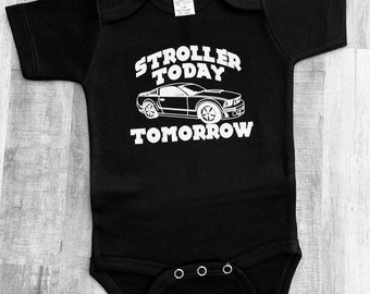 Può includere: Body nero per neonato con testo bianco che recita "Stroller Today, Tomorrow". Sopra il testo è presente una silhouette bianca di un'auto.