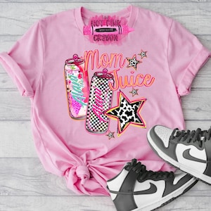 May include: Pink t-shirt with the text "Mom Juice" and graphics of two beverage cans and a star. One can has a floral design, the other a black and white checkerboard pattern. A pair of black and white sneakers are at the bottom.