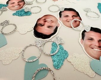 May include: A collection of confetti featuring images of men's faces, silver glitter rings, and blue and white glitter clouds.