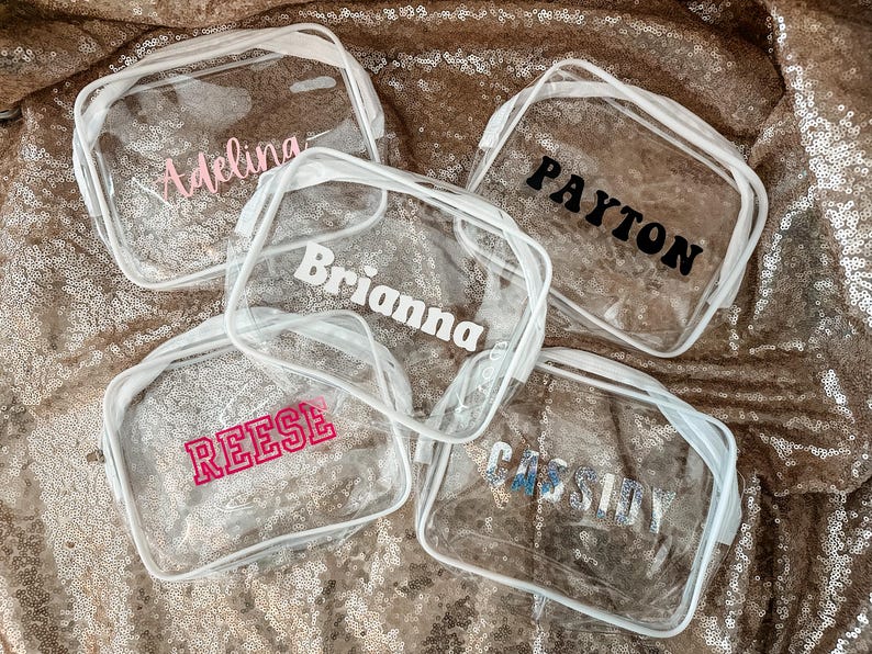 May include: Four rectangular clear plastic pouches with white zippers. Each pouch features a personalized name printed on the front: Adelina in light pink, Payton in black, Brianna in white, Reese in hot pink, and Cassidy in silver glitter.