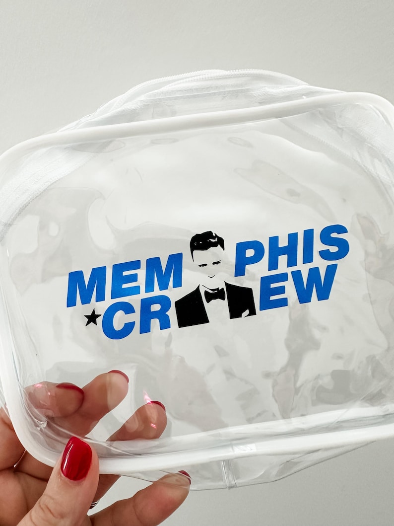 May include: A clear, rectangular vinyl pouch with white trim and a zipper closure. The front features blue text that reads MEMPHIS CREW, with a black and white graphic of a person in a tuxedo jacket and bowtie positioned between the words.