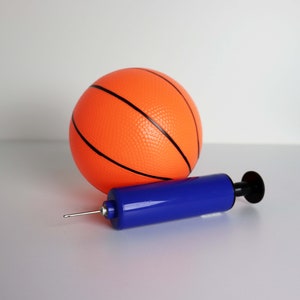 May include: An orange basketball with black lines and a blue hand pump. The basketball is round and has a textured surface. The pump is blue with a black handle and a silver needle.