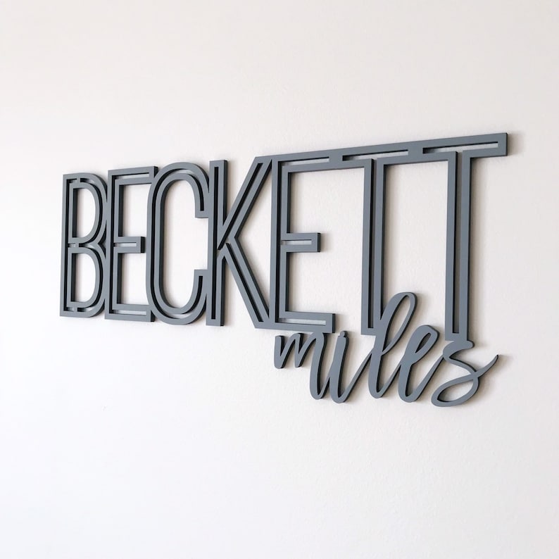 Puede incluir: Decoraci&oacute;n de pared de madera gris con el nombre "Beckett" en letras en negrita superpuestas y la palabra "miles" en escritura cursiva.