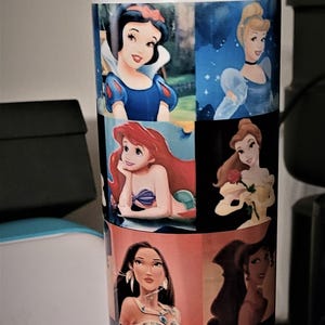 May include: A tall water bottle featuring images of Disney princesses. The bottle has a blue base and a yellow handle. The princesses include Snow White, Cinderella, Ariel, Belle, Pocahontas, Tiana, and Elsa.