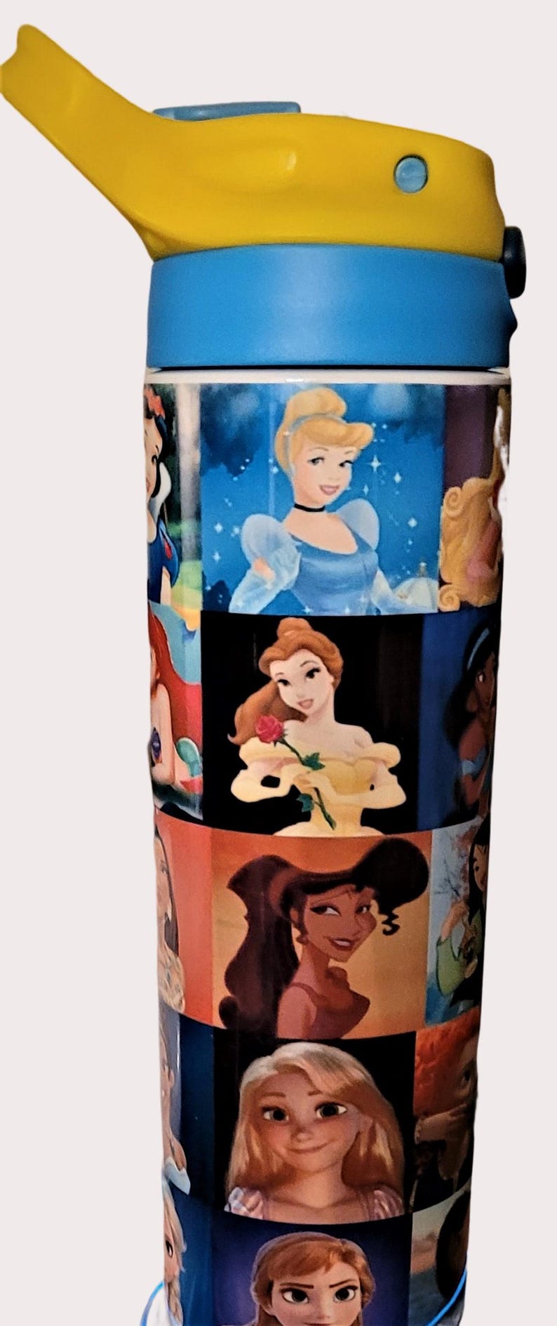 May include: A blue and yellow water bottle featuring images of Disney princesses. The bottle has a blue base and a yellow flip-top lid. The images include Cinderella, Belle, and Jasmine.