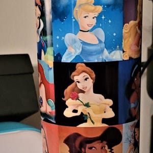 May include: A blue and yellow water bottle featuring images of Disney princesses. The bottle has a yellow flip-top lid and a blue base. The body of the bottle is covered in colorful images of Cinderella, Belle, and other Disney princesses.