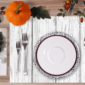 Puede incluir: Un mantel individual blanco de imitaci&oacute;n de madera con un plato blanco, un tenedor, una cuchara y un cuchillo. El mantel individual tiene un aspecto desgastado con pintura blanca sobre un patr&oacute;n de veta de madera. Hay una peque&ntilde;a calabaza y una rama de hojas en el fondo.