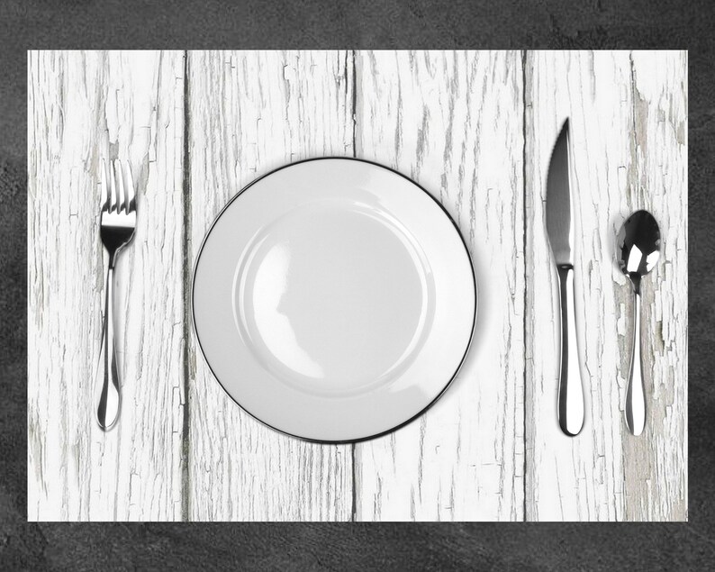 Puede incluir: Un plato de cena de cer&aacute;mica blanca con un borde negro se encuentra sobre una mesa de madera blanqueada. Un tenedor, un cuchillo y una cuchara se colocan alrededor del plato.