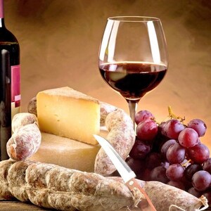 Peut inclure: Un verre de vin rouge, une bouteille de vin rouge, une grappe de raisin rouge, un couteau et une sélection de fromage et de charcuterie sur une table en bois.